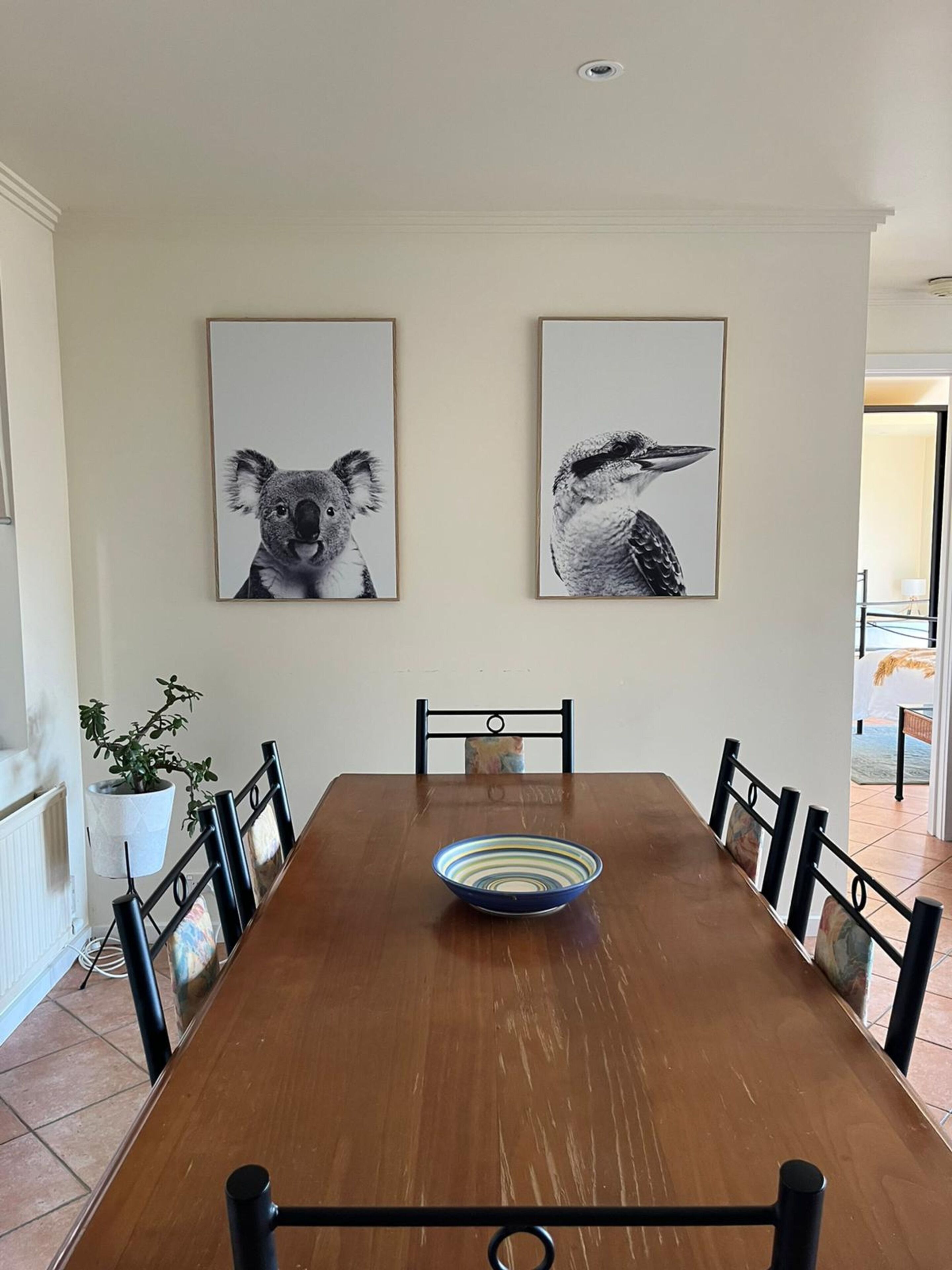 A dining room with a wooden table, chairs, and two framed animal pictures on the wall.