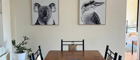 Une salle à manger avec une table en bois, des chaises et deux tableaux représentant des animaux, accrochés au mur.