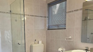 Un bagno con cabina doccia in vetro, un water, un lavandino e una finestra con persiane.