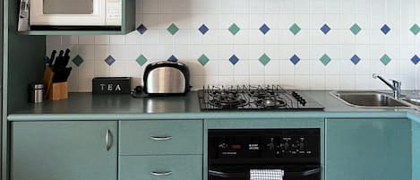 Une cuisine avec des meubles de couleur turquoise, un four à micro-ondes, une cuisinière à gaz et un lave-vaisselle.