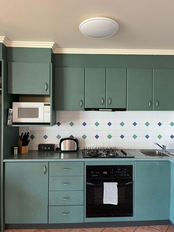 Une cuisine avec des meubles de couleur turquoise, un four à micro-ondes, une cuisinière à gaz et un lave-vaisselle.