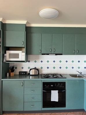 A kitchen with teal cabinets, a microwave, a gas stove, and a dishwasher. - Vista Di Mare (Lorne)