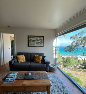 A modern living room with a sofa, a coffee table, and a large window offering a view of the sea. - Vista Di Mare (Lorne)