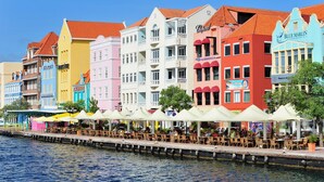 A waterfront promenade with colorful buildings, outdoor seating, and a dock extending into the water. - Fully renovated Tropical 3-bdr Villa at Blue Bay Resort, at beach and pool!!! (Blue Bay)