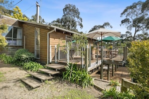 A wooden house with a deck, outdoor seating, and a covered area with an umbrella.