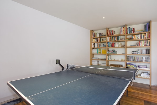 A room with a ping pong table, a bookshelf filled with books, and a small table with a device.
