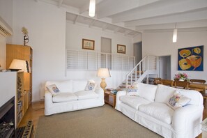 A spacious living room with white sofas, a wooden cabinet, and a staircase leading to another level.
