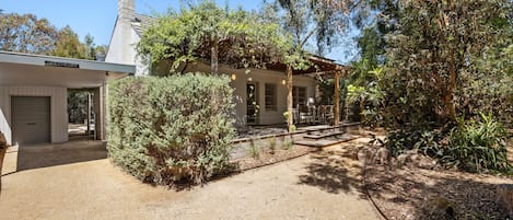 A building with a covered patio area, a gravel driveway, and surrounding vegetation.