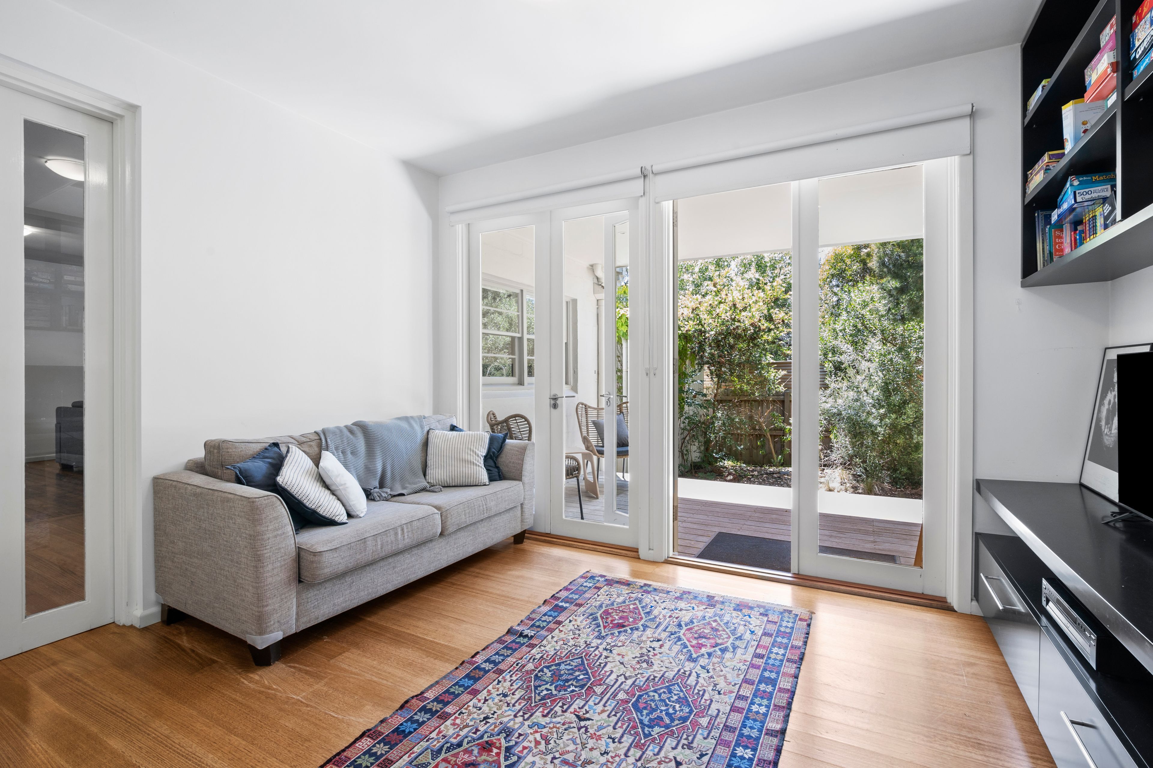 Ein Wohnzimmer mit grauem Sofa, einem gemusterten Teppich und einer Schiebetür zu einem Außenbereich.