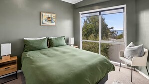 Un dormitorio con una cama grande, una ventana con vistas, una silla y un cuadro en la pared.