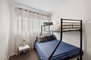 Une chambre avec un lit superposé, une petite table de chevet et une lampe.