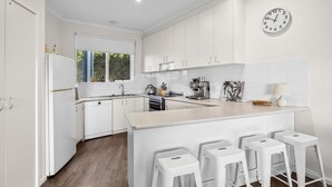 Una cocina moderna con armarios blancos, una isla central con taburetes de bar, una cafetera y un reloj en la pared.