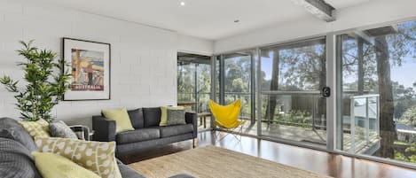 Una sala de estar moderna con un sofá gris, un sillón amarillo y un ventanal con vistas a árboles.