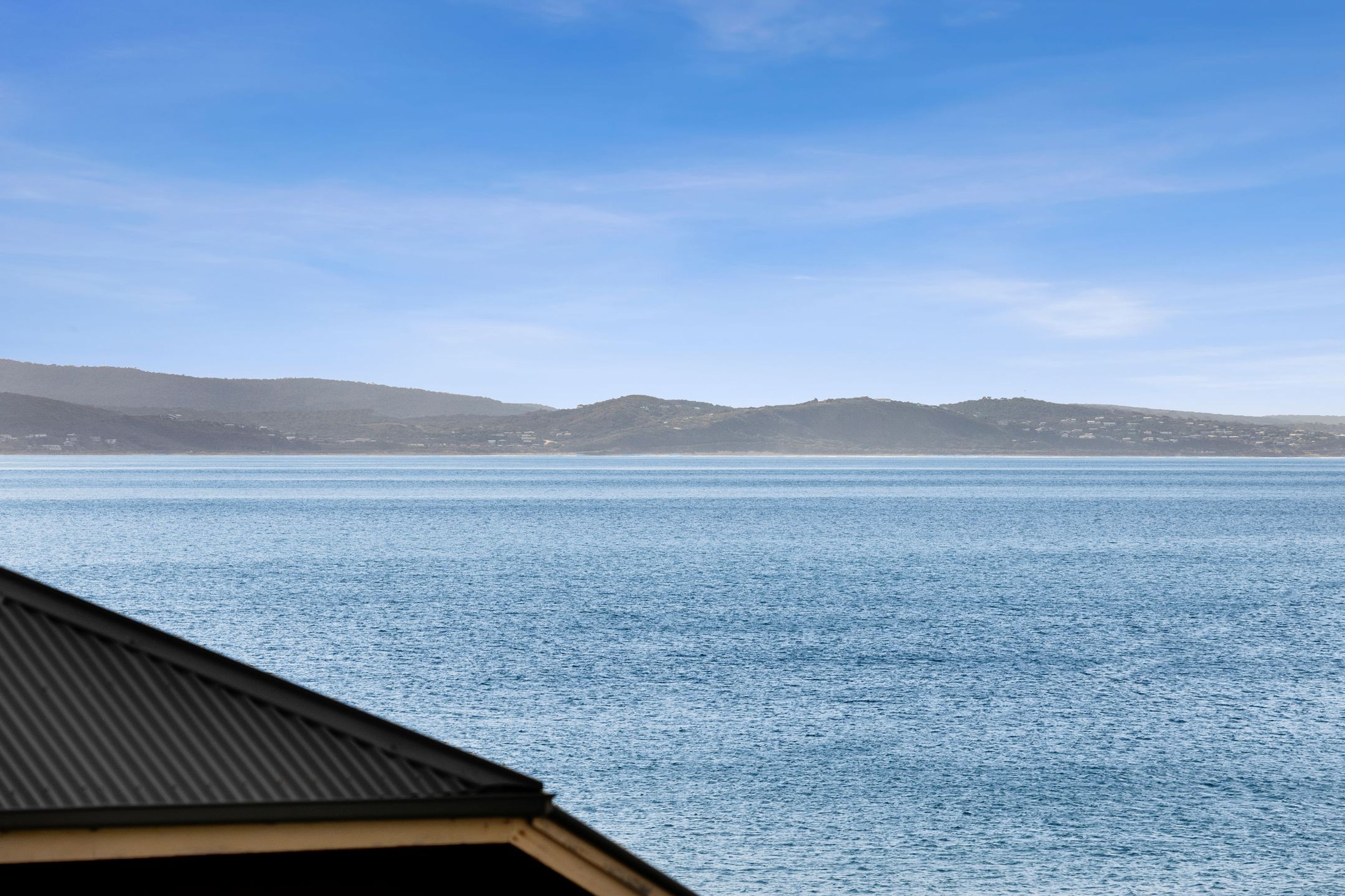 A coastal view with a clear sky, calm sea, and distant hills.