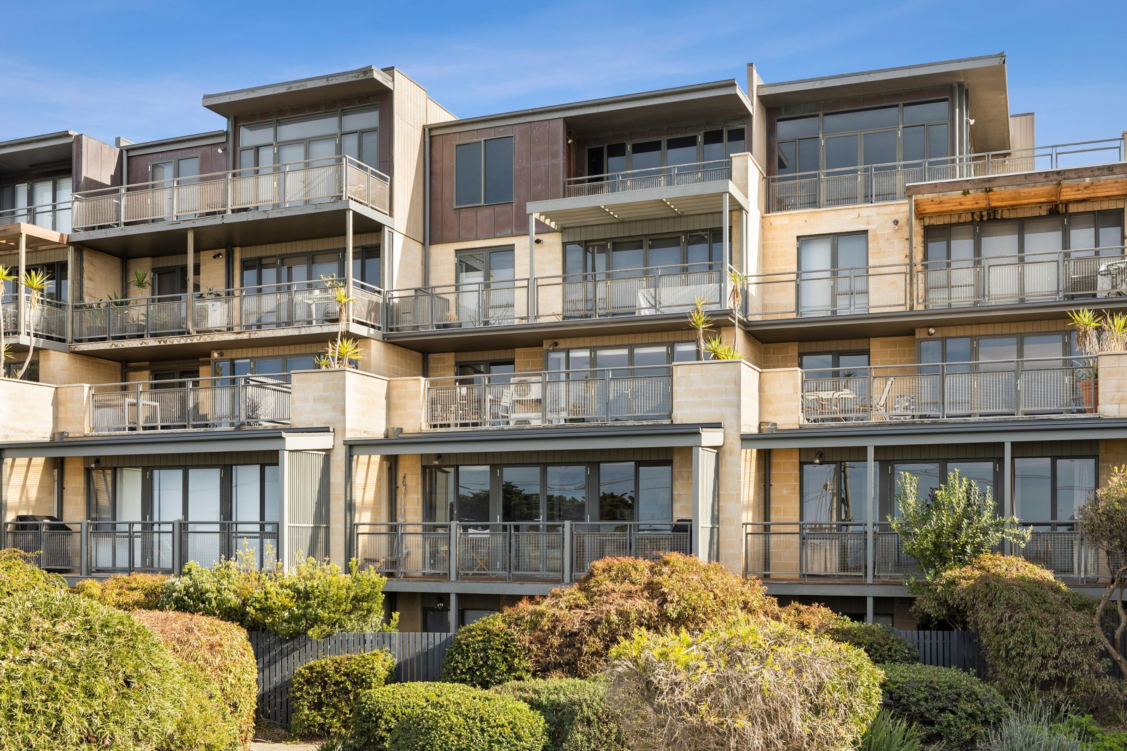 A multi-story residential building with balconies, large windows, and a well-maintained garden.