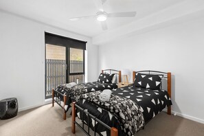 A bedroom with two beds, a ceiling fan, a window with a view, and a small bedside table with a lamp.