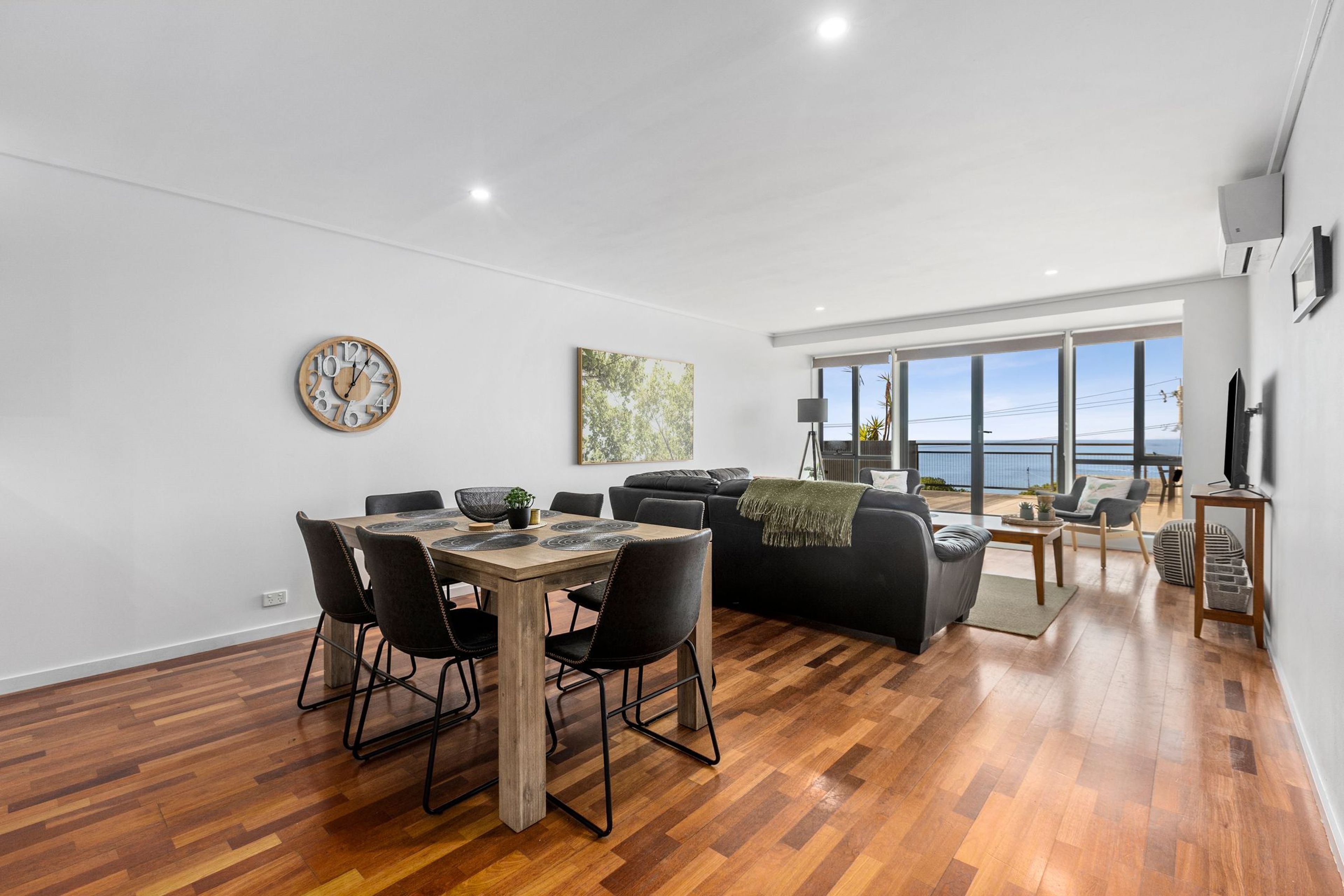 A modern living space with a dining area, a sofa, and a large window offering a view.