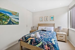 Une chambre à coucher avec un lit, deux tables de chevet, une fenêtre et trois tableaux encadrés accrochés au mur.