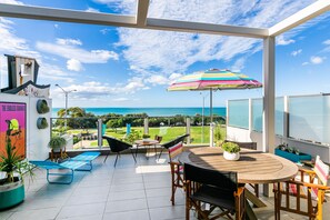 Un balcon spacieux avec vue sur la mer, un parasol rayé aux couleurs vives et une table avec des chaises.