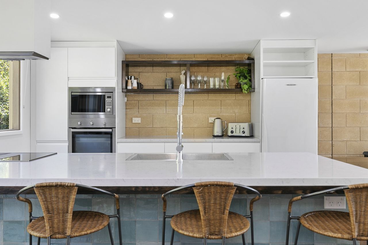 Een moderne keuken met een centraal eiland, roestvrijstalen apparatuur en een achterwand van baksteen.