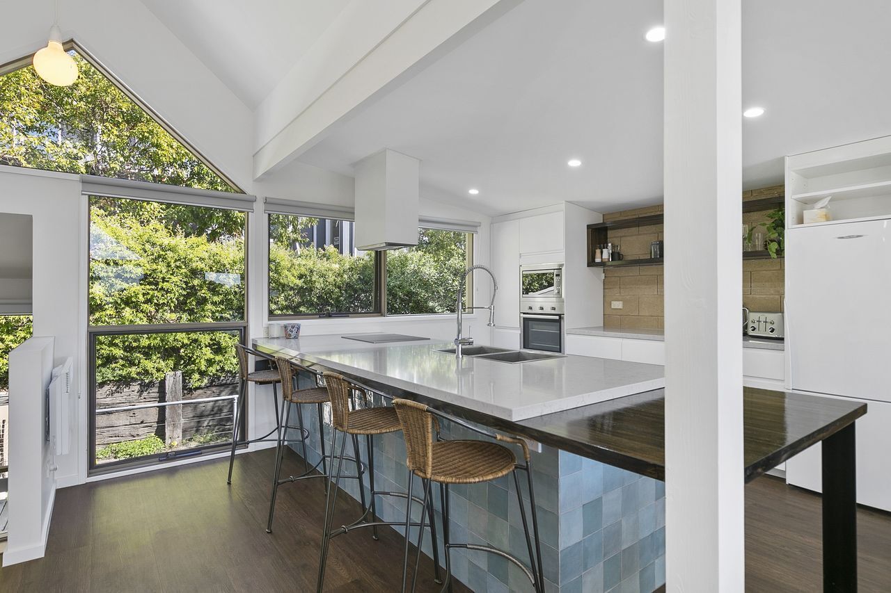 Een moderne keuken met een groot eiland, barstoelen en uitzicht op groen.