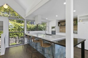 A modern kitchen with a large island, bar stools, and a view of greenery outside.