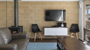 A living room with a fireplace, a flat-screen TV, a white cabinet, and two black chairs. - Lorne Lodge (Lorne)