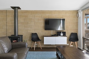 Ein Wohnzimmer mit Kamin, Flachbildfernseher, einem weißen Schrank und zwei schwarzen Sesseln.