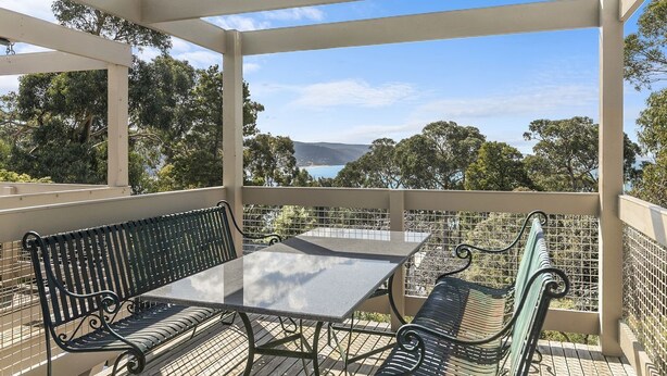 An outdoor patio with a table and two benches, overlooking a scenic landscape with trees and a distant view. - Lorne Lodge (Lorne)