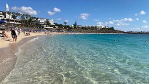 Una playa con agua cristalina, gente y edificios al fondo.