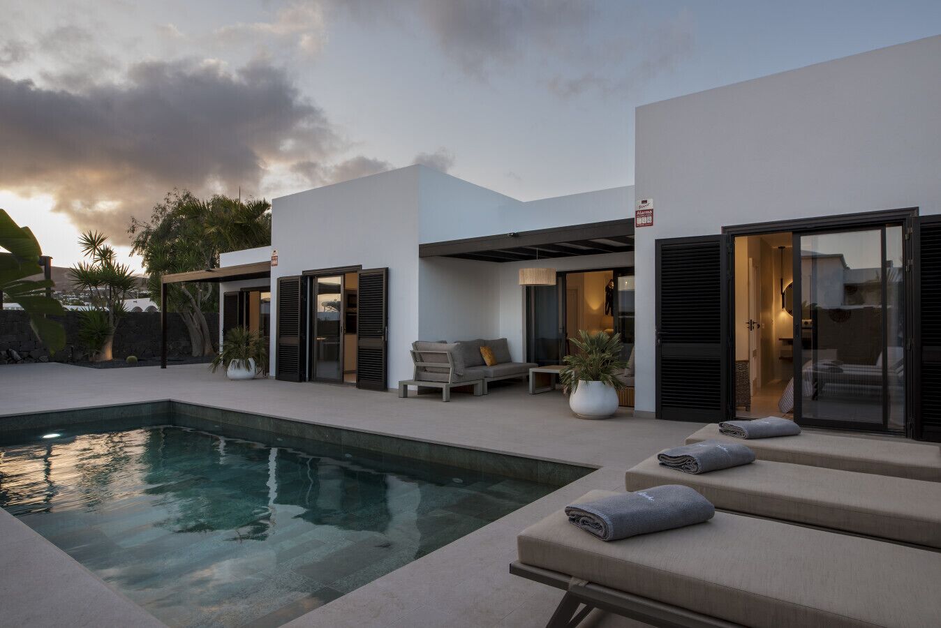 A modern outdoor pool area with a clear pool, a lounge chair, and a small seating area.
