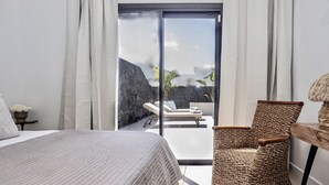 Un dormitorio con una cama, una silla de mimbre, una mesa y vistas a un muro de piedra y plantas.