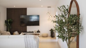 Una sala de estar moderna con un sofá blanco, un televisor de pantalla plana montado en la pared, un aparador de madera y un espejo grande.