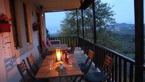 An outdoor dining area with a wooden table and chairs, a candle, and a view of the landscape.