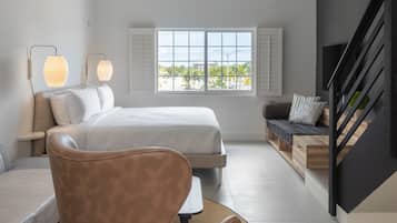 A modern bedroom with a bed, a seating area, a staircase, and large windows.