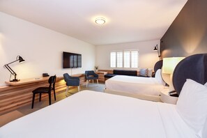 Habitación de hotel con dos camas, un escritorio con silla, televisor, ventana y lámpara.