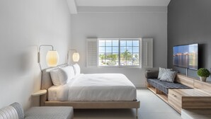 Un dormitorio moderno con cama, mesitas de noche, televisión y ventana con vista a la ciudad.