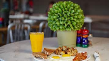 Ein Frühstücksteller mit Eiern, Toast und Kartoffeln, ein Glas Orangensaft und ein kleiner Topfpflanzen auf einem Marmortisch.