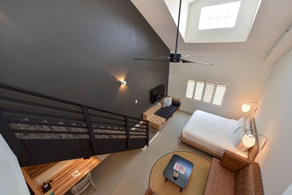 A modern loft-style bedroom with a skylight, a bed, a desk, and a staircase.