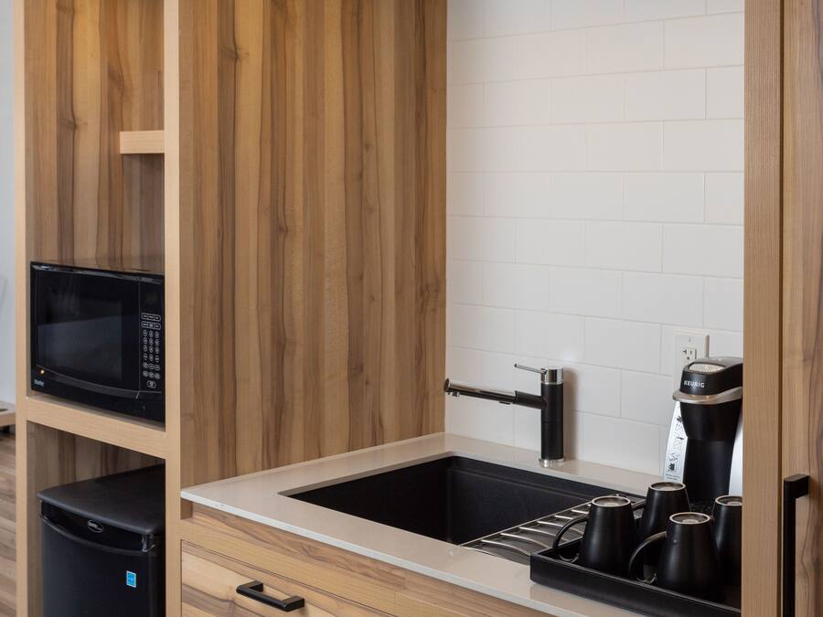 Una cocina moderna con armarios de madera, un microondas negro, una cafetera y un fregadero.