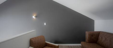 A modern room with a sloped ceiling, a brown leather sofa, a brown leather armchair, and a small wall-mounted light fixture.
