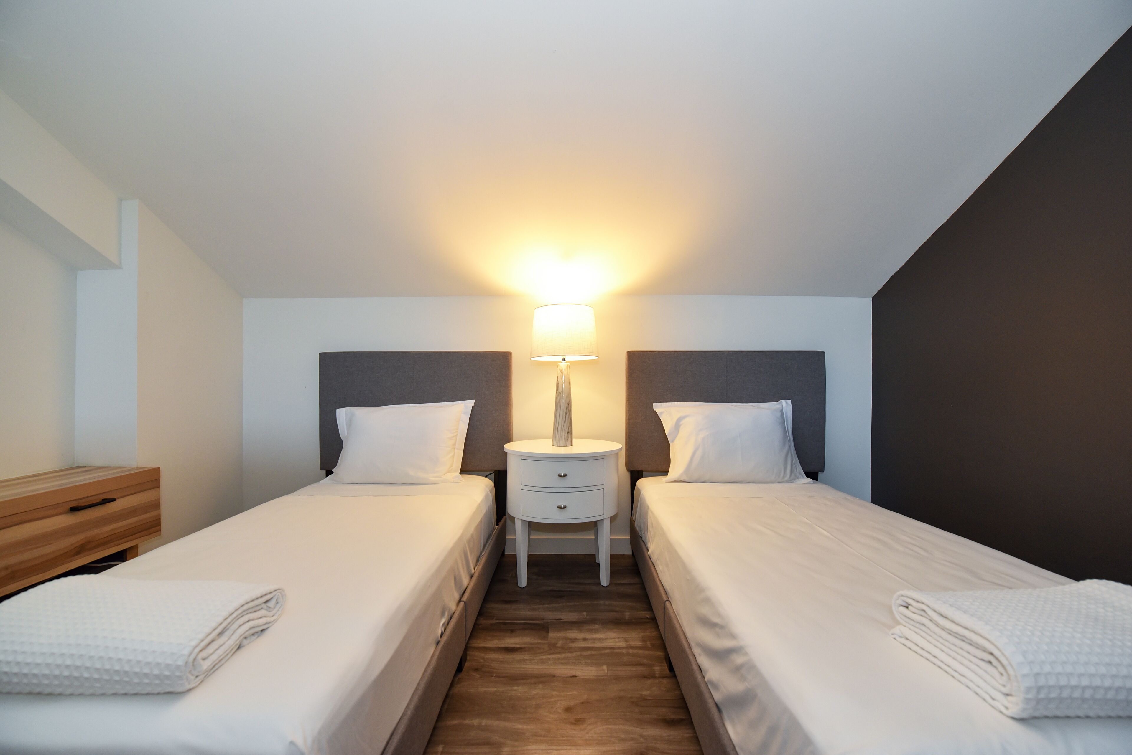 A twin room with two beds, a bedside table, a lamp, and a wooden nightstand.