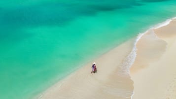 A beach with clear turquoise water and a person walking along the shore.