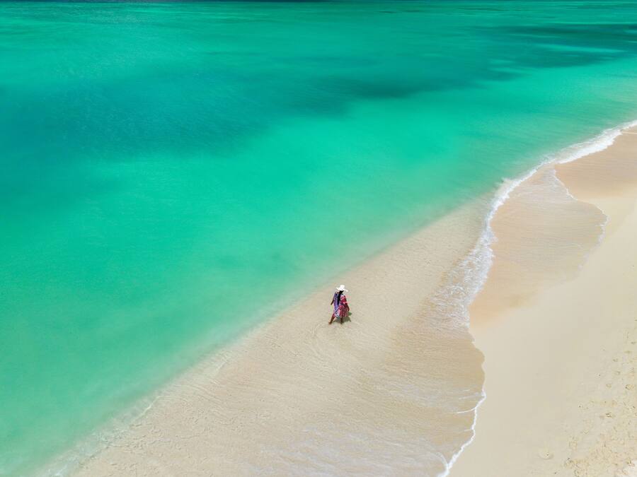 A beach with clear turquoise water and a person walking along the shore.