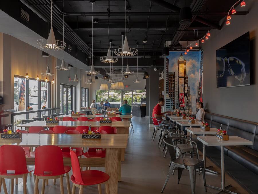 A modern restaurant interior with high tables, red chairs, and pendant lighting.
