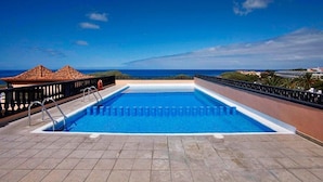 Une piscine sur le toit avec une eau d’un bleu cristallin, une terrasse carrelée et une vue sur l’océan.