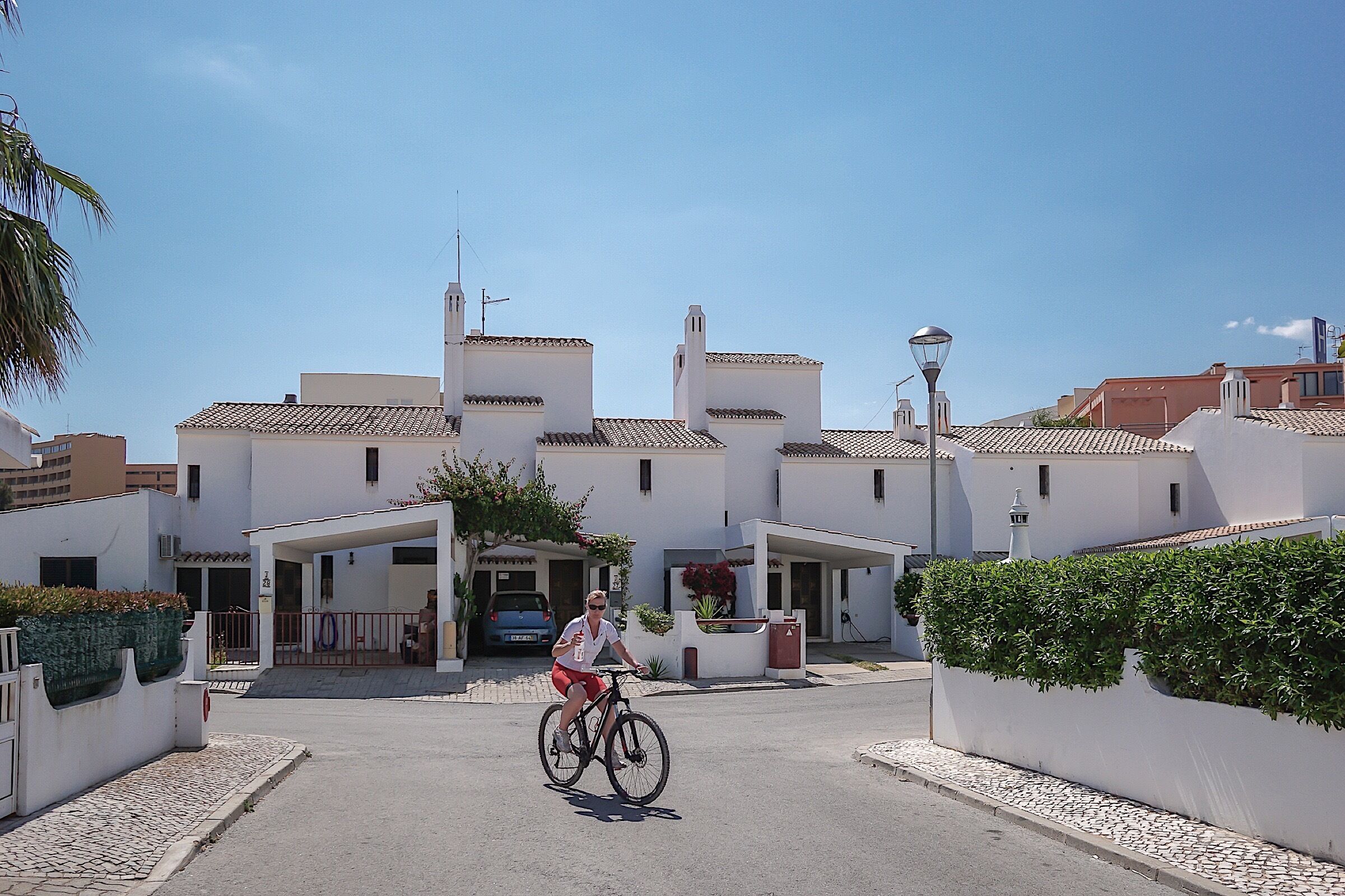 A residential street with white houses, a cyclist, and a parked car.