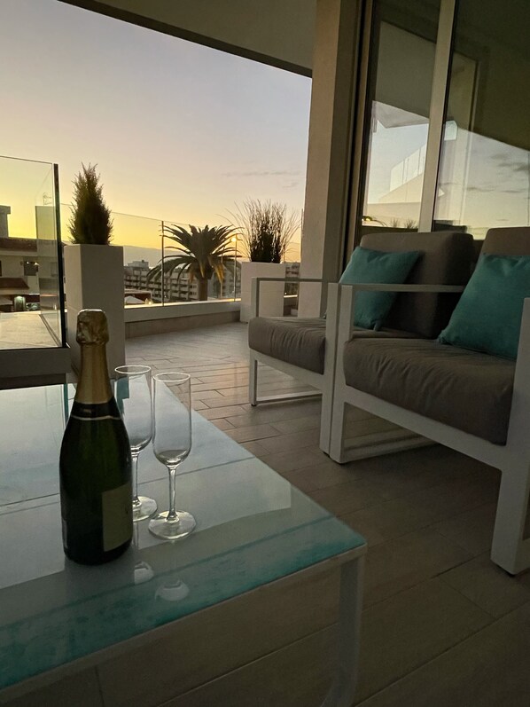 En modern utomhusplats med sittmöbler, ett glasbord, en flaska champagne och två glas.
