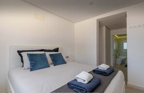 A modern hotel room with a neatly made bed, a bedside table, and a view into the bathroom.