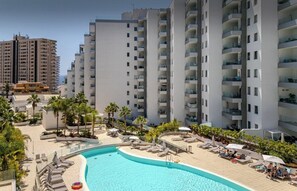 A modern hotel with a central swimming pool surrounded by lounge areas and palm trees.